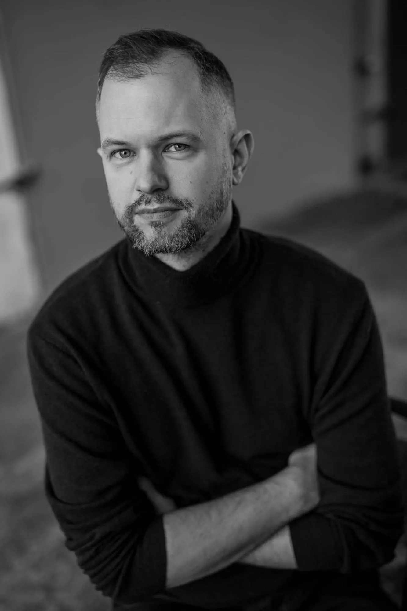 Tomasz Żółtak w czarnym golfie, ze skrzyżowanymi rękami, lekko się uśmiecha